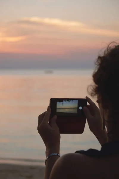 stock image Woman photographs the sunset on the sea by smartphone