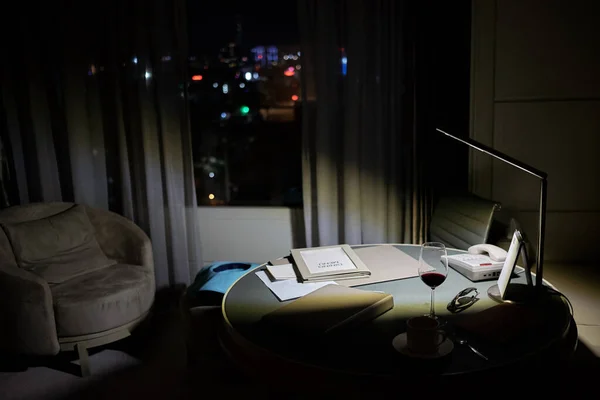 Interior at the room with working table, armchair and large window with night city view.