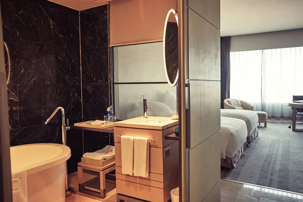 Интерьер гостиничного номера с ванной и спальней с двумя кроватями и большим окном над стеной — стоковое фото