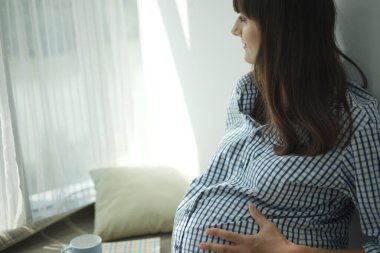 Kareli gömlekli mutlu hamile kadının kanepeye oturup gözlerini kaçırdığı yakın plan.