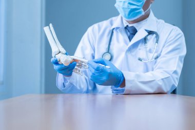 Yakın plan eldiven giyen tıp eldivenli doktor hastanede ayağın yapay kemiğini tutuyor..