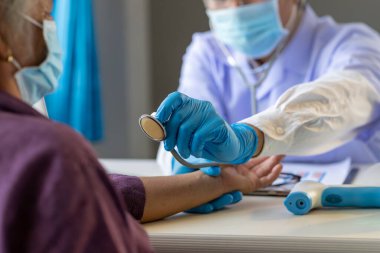 Asyalı doktor steteskop kullanarak hastanın akciğerini dinliyor, yaşlı sağlık kontrolü yapıyor, cerrahi maske takıyorlar Corona virüsü covid-19 enfeksiyonu riski olan yaşlı kadın hasta.