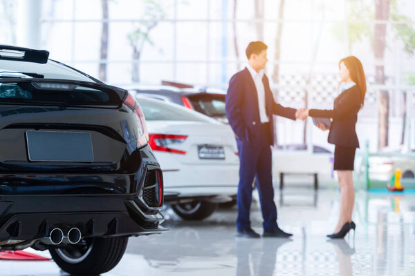 Selective focus on a new car and blur the dealership professional salesman and his client shaking hands. concept professionalism agreement contract leasing renting retail car sales .