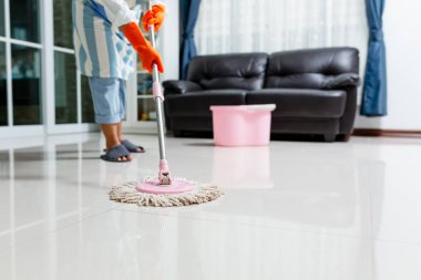 Evdeki yerleri temizlerken ıslak bez kullanan koruyucu eldivenli Asyalı güzel bir genç kadın evi temizlemek için paspas kullanıyor..