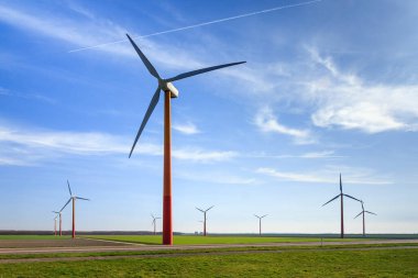 Hollanda 'da mavi gökyüzü olan bir arazide yeşil sürdürülebilir enerji için çoklu modern yel değirmenleri türbinleriyle güzel manzara.