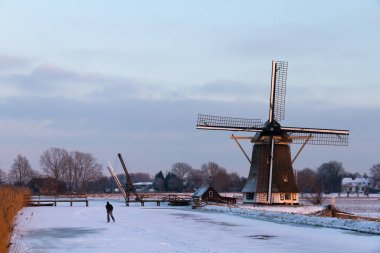 Hollanda 'da Baambrugge yakınlarında gün batımında nehirde buzla kaplı güzel bir yel değirmeni.