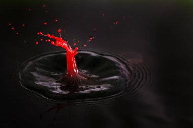 Bir damla kırmızı kremanın küçük bir adamın vurulması şeklinde karanlık suya düşüşünün güzel bir görüntüsü.