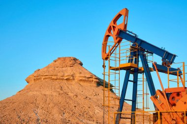 Oil pump are working in the blue sky background. World Oil Industry. Western region of Kazakhstan.A oil pump is the overground drive for a reciprocating piston pump in an oil well. clipart