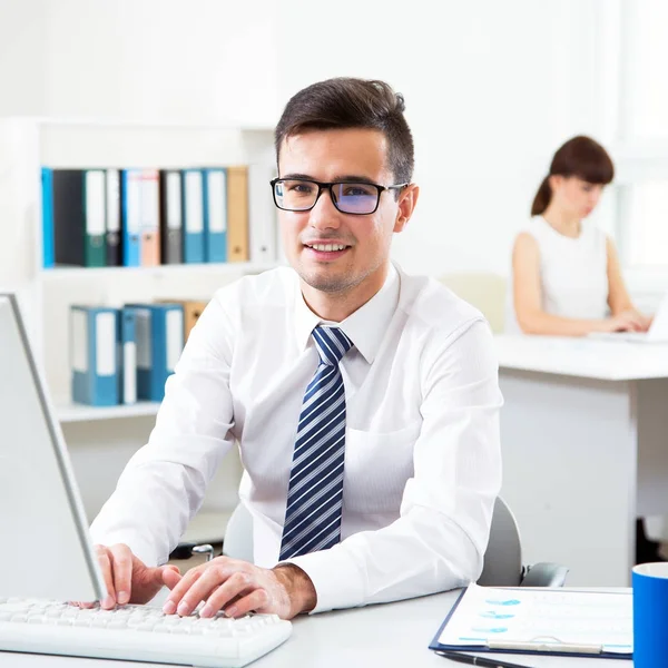 Joven Hombre Negocios Guapo Sonriendo Cámara Cuando Utiliza Ordenador Oficina —  Fotos de Stock