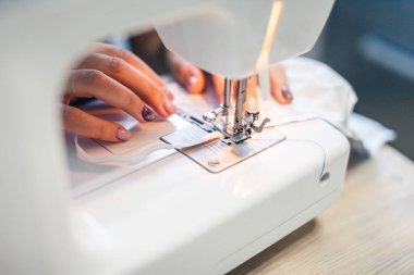 Genç kadın elleri dikiş makinesinde. Kız evde şık şeyler dikiyor..