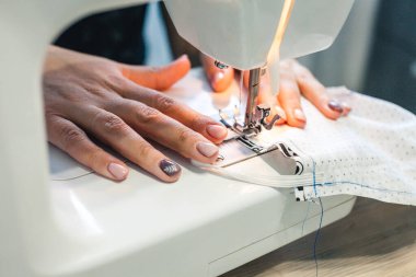 Genç kadın elleri dikiş makinesinde. Kız evde şık şeyler dikiyor..