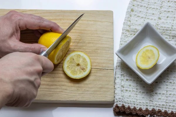 Eski ahşap masada ve beyaz arka planda limon dilimleri kesen eller.