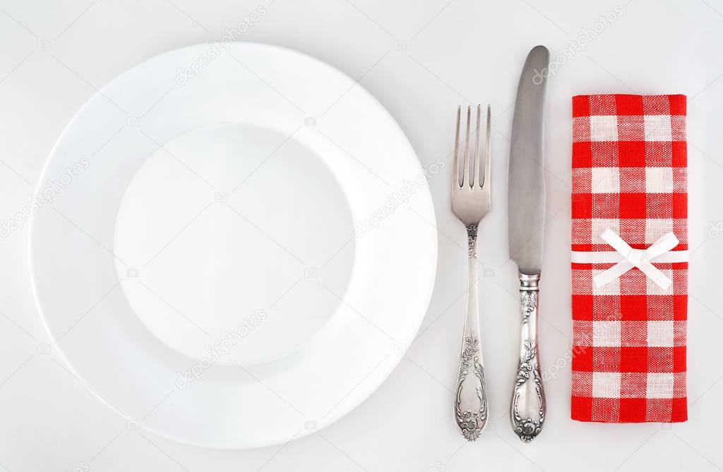 Empty plate with cutlery and red checkered napkin.