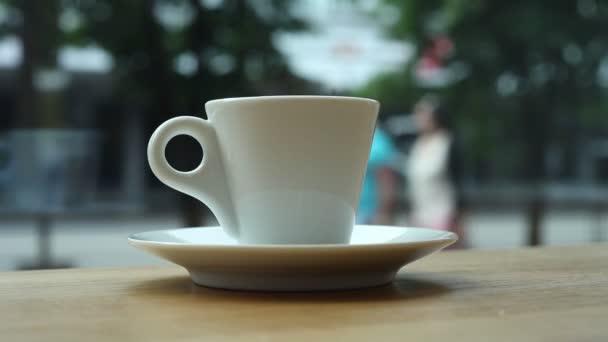 A cup of coffee on a table in a cafe by the window on the background of people and cars. — Stock Video