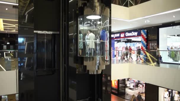 Minsk, Weißrussland, 9. Juli 2017: Menschen fahren in einem gläsernen Fahrstuhl im Hintergrund der Geschäfte in der Mall "-Galerie" — Stockvideo