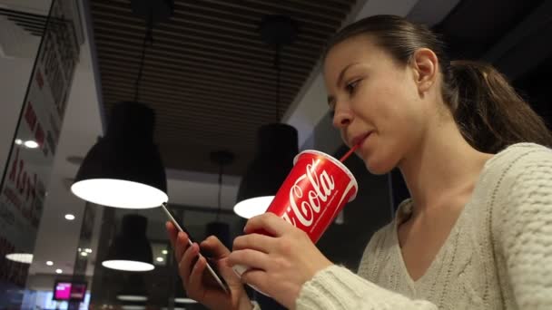 可口可乐软饮料。女人喝可口可乐，在咖啡店里用智能手机。白俄罗斯明斯克- 2017年10月 — 图库视频影像