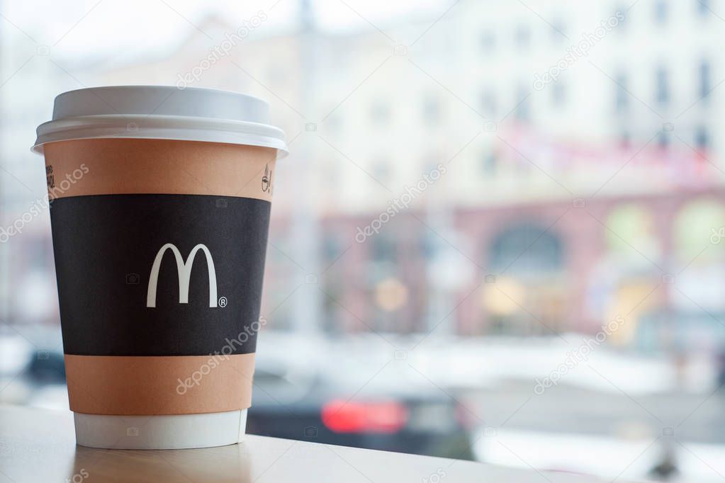 Minsk, Belarus, February 18, 2018: Paper cup of coffee with McDonald's logo on table near window on background of city in McDonald's restaurant