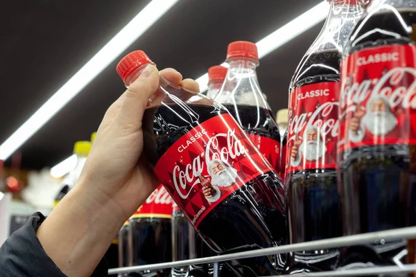 Minsk, Belarus - 19 Aralık 2019: etiketinde Noel Baba resmi olan bir şişe Coca-Cola tutuyor. Bakkalda Coca-Cola satan adam..