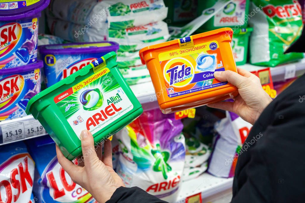 MINSK, BELARUS - February 2, 2020: Buyer chooses which washing powder to buy. Washing powder of different brands Ariel and Tide in hands of buyer.