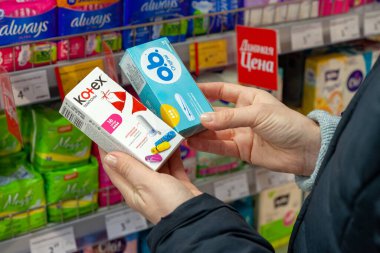 Minsk, Belarus - 2 Şubat 2020: Kadın süpermarketten hijyen koruması satın alıyor. Alıcı hangi tamponu alacağını seçer. Kotex ve O.B. 'nin farklı marka tamponları. ellerde.