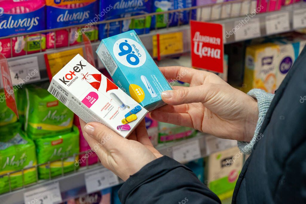 MINSK, BELARUS - February 2, 2020: Woman buys hygiene protection in a supermarket. Buyer chooses which tampons to buy. Tampons of different brands Kotex and O.B. in hands.
