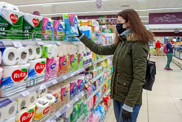 MINSK, BELARUS - 27 Nisan 2020: Koruyucu maskeli bir alıcı koronavirüs salgını sırasında süpermarkette tuvalet kağıdı seçer. Pardemik sırasında alışveriş.