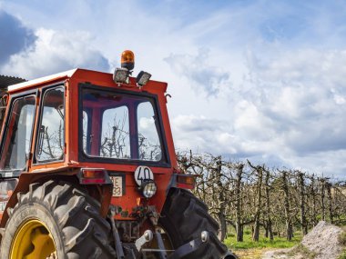Ön planda yaprakları olmayan kırmızı traktör ve çok tehditkar bulutlar, yatay fotoğraf en kapalı görüş açısı.