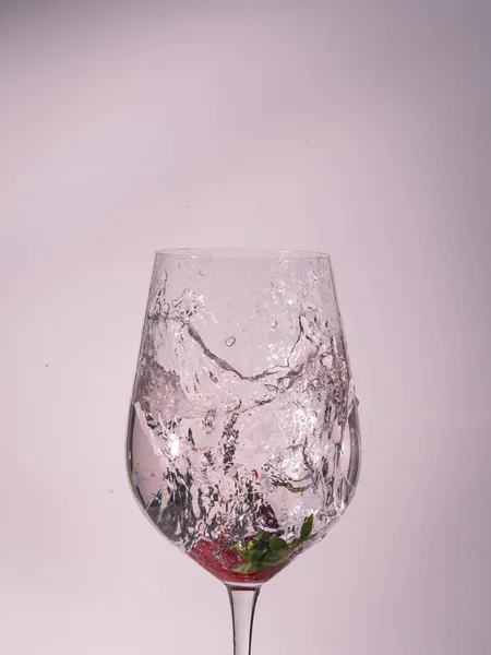 Meyveye düşen ve suyun hareketini donduran su dolu bir bardağın beyaz arkaplan görüntüsü