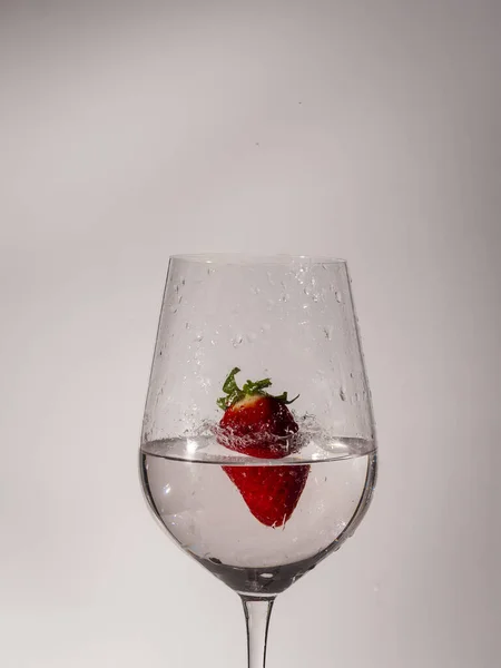 Sulu bir bardağın beyaz arkaplanlı görüntüsü. Çilek suya düşer ve suyun içindeki hareketi dondurur.