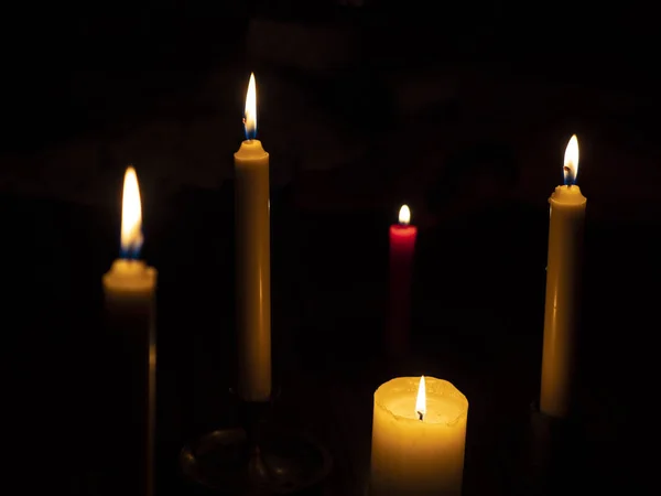 Farklı boyutlarda mumlar yakıyor ön plandaki muma ve bir kırmızı muma odaklanıyor.