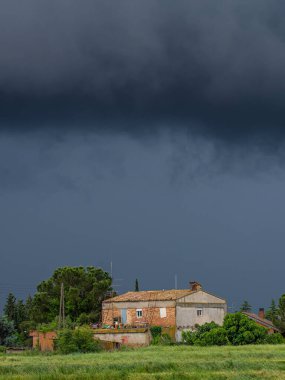 Koyu bulutlu dikey fotoğraf, ağaçlı eski ev ve yeşil çayır