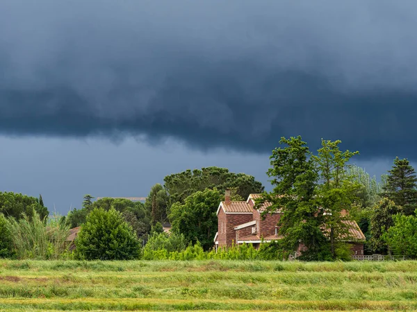 Horizontal photo with dark clouds, tree-covered house and green meadow
