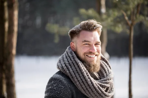 Glimlachende man in winter jas kijken camera in bos — Stockfoto