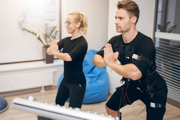 Deportista en traje ems y su entrenador personal en pose de yoga — Foto de Stock