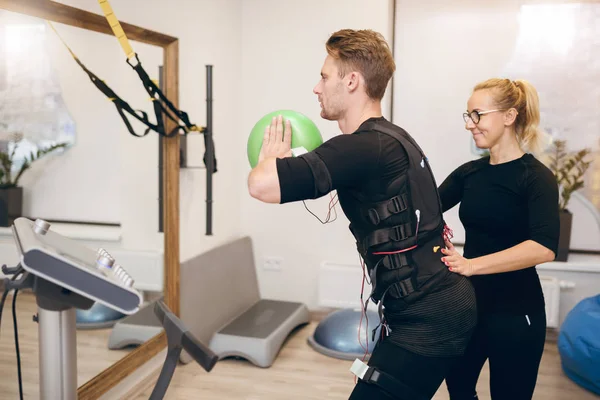 Sportsman doing ems training with coach in front of mirror