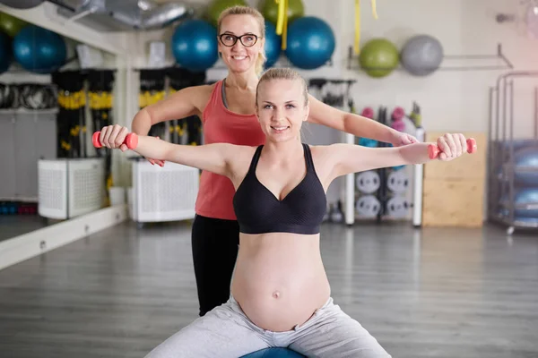 Happy pregnant woman lifting weights with her personal coach — Stock Photo, Image