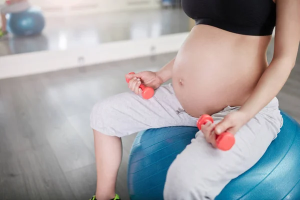 Kobieta w ciąży, siedząc na piłka treningowa wagi gospodarstwa — Zdjęcie stockowe