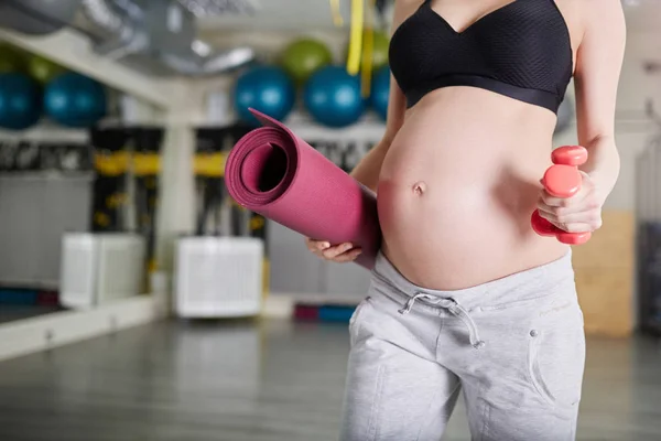 Kobieta w ciąży siłowni trzyma wagi i mat — Zdjęcie stockowe