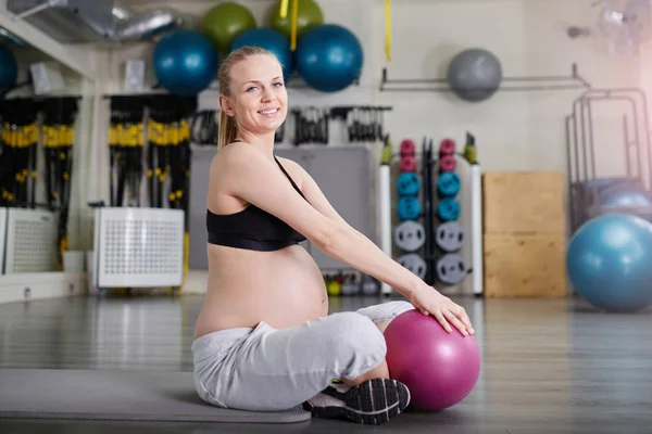 Szczęśliwa Kobieta w ciąży, siedząc w siłowni z pilates ball — Zdjęcie stockowe