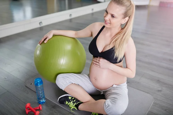 Uśmiecha się kobieta w ciąży, siedząc na siłowni mata z pilates ball — Zdjęcie stockowe