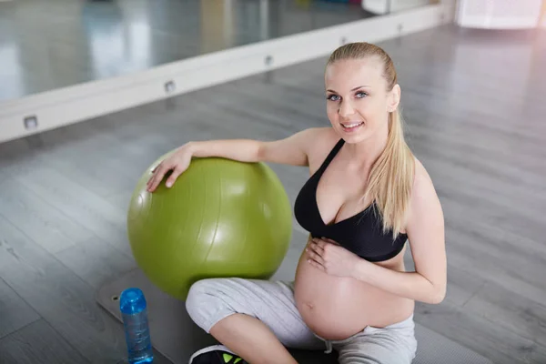 Dość ciężarna kobieta siedzi na siłowni mata z pilates ball — Zdjęcie stockowe