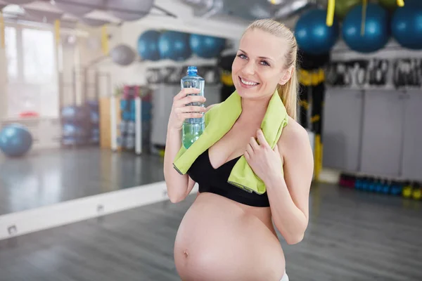 Piękna kobieta w ciąży uśmiechający się w siłowni, trzymając butelkę i ręcznik — Zdjęcie stockowe