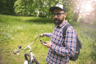Hipster adam Bisiklet telefon kullanarak Park'ta ayakta