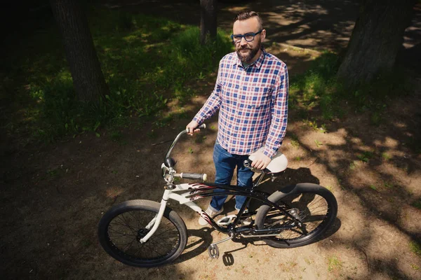 Moderne jongeman permanent in park holding stuur van de fiets — Stockfoto