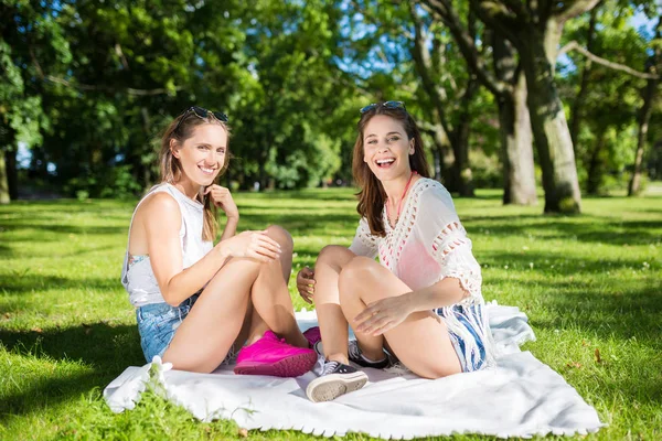Glückliche Freundinnen sitzen auf Decke im Park — Stockfoto