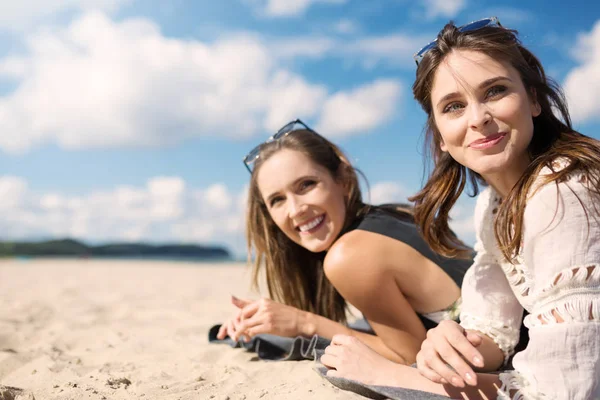 Mulheres bonitas deitadas na praia rindo olhando para longe — Fotografia de Stock