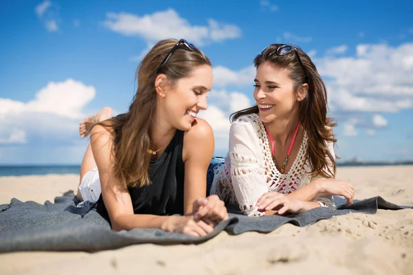Zwei schöne Freundinnen lachend am Strand liegen — Stockfoto