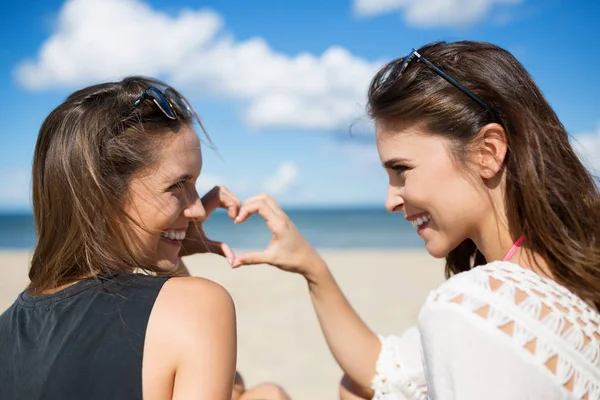 Zwei schöne Frauen am Strand, die Herzform zum Lachen bringen — Stockfoto