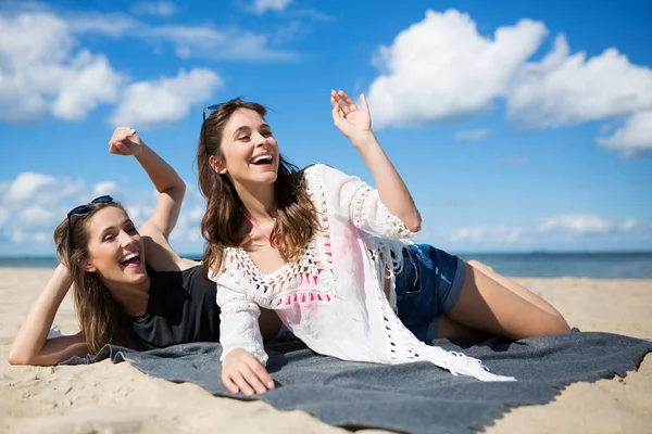 Dos mujeres jóvenes tumbadas en la playa saludando y riendo — Foto de Stock