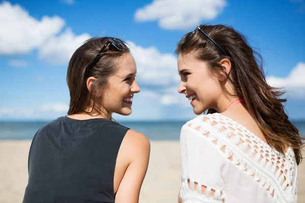 Zwei schöne Frauen am Strand, die einander lachend anschauen — Stockfoto